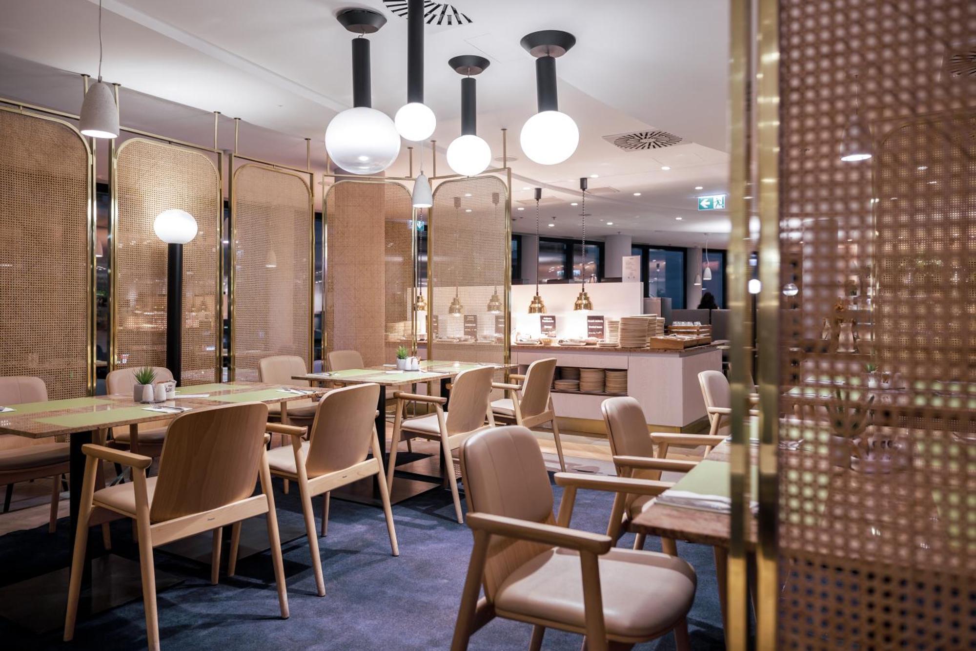 Radisson Blu Resort Świnoujście Εξωτερικό φωτογραφία The photo shows a modern restaurant interior. There are wooden tables and chairs arranged neatly. The atmosphere appears warm and inviting, with soft lighting provided by round pendant lamps hanging from the ceiling. Partitions made of woven material