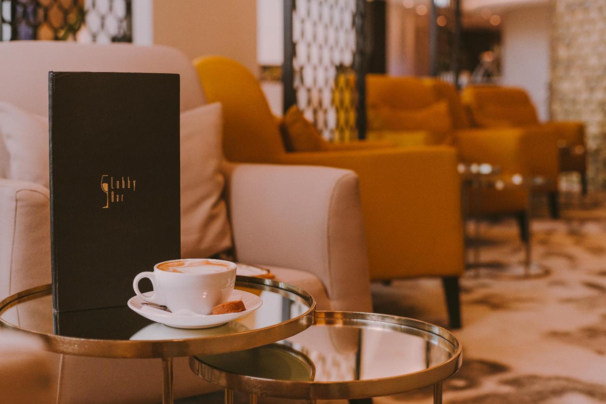 Radisson Blu Resort Świnoujście Εξωτερικό φωτογραφία The photo shows a cozy indoor setting with a stylish, modern atmosphere. In the foreground, there is a small round glass table with a white coffee cup and a saucer, alongside a small biscuit or cookie. Next to the coffee, there is a black menu with e