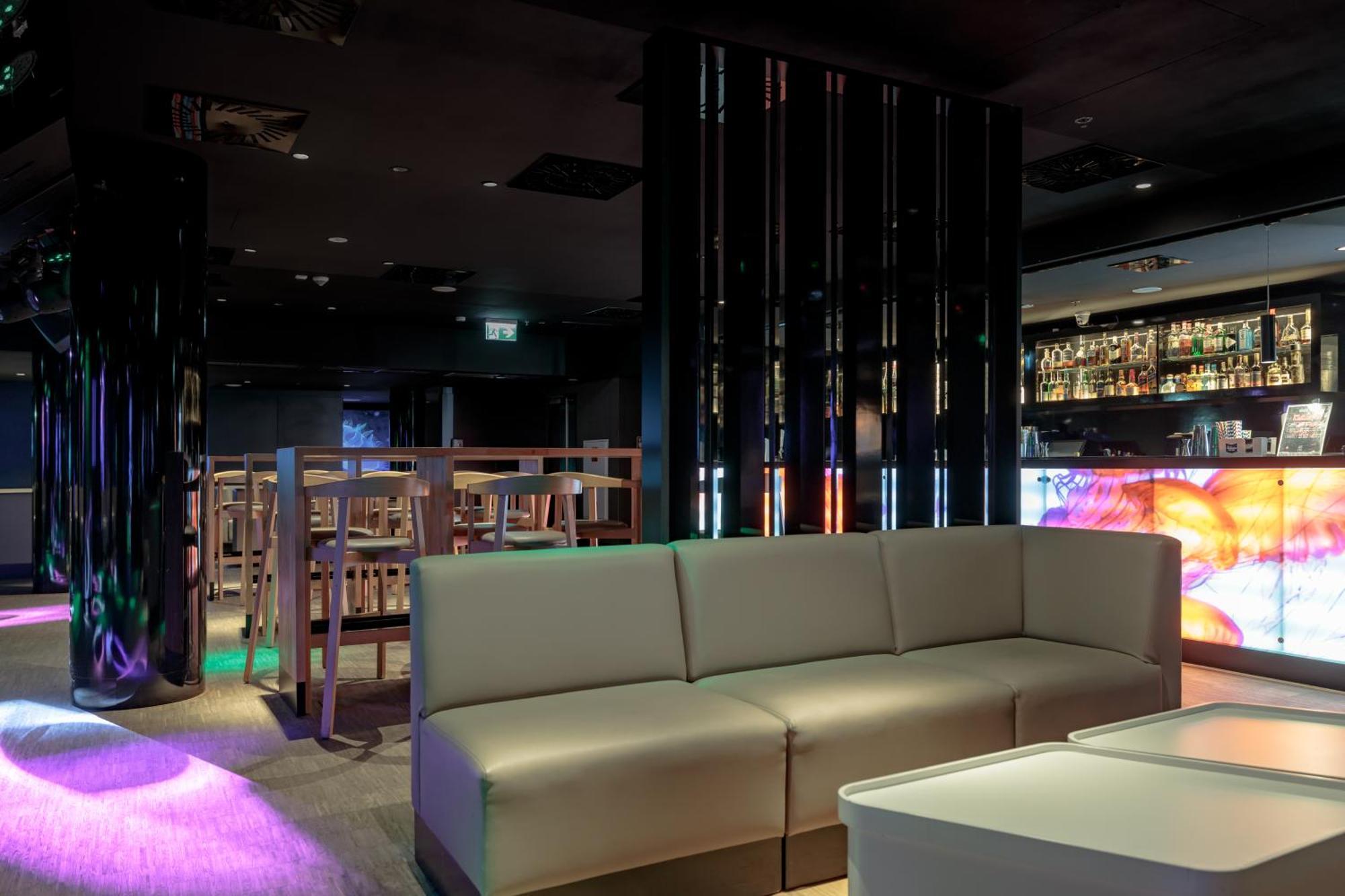 Radisson Blu Resort Świnoujście Εξωτερικό φωτογραφία The photo shows the interior of a stylish lounge or bar. The space features a modern design with dark walls and a sleek atmosphere. There is a beige sectional sofa in the foreground, providing a casual seating area. In the background, a bar is visibl