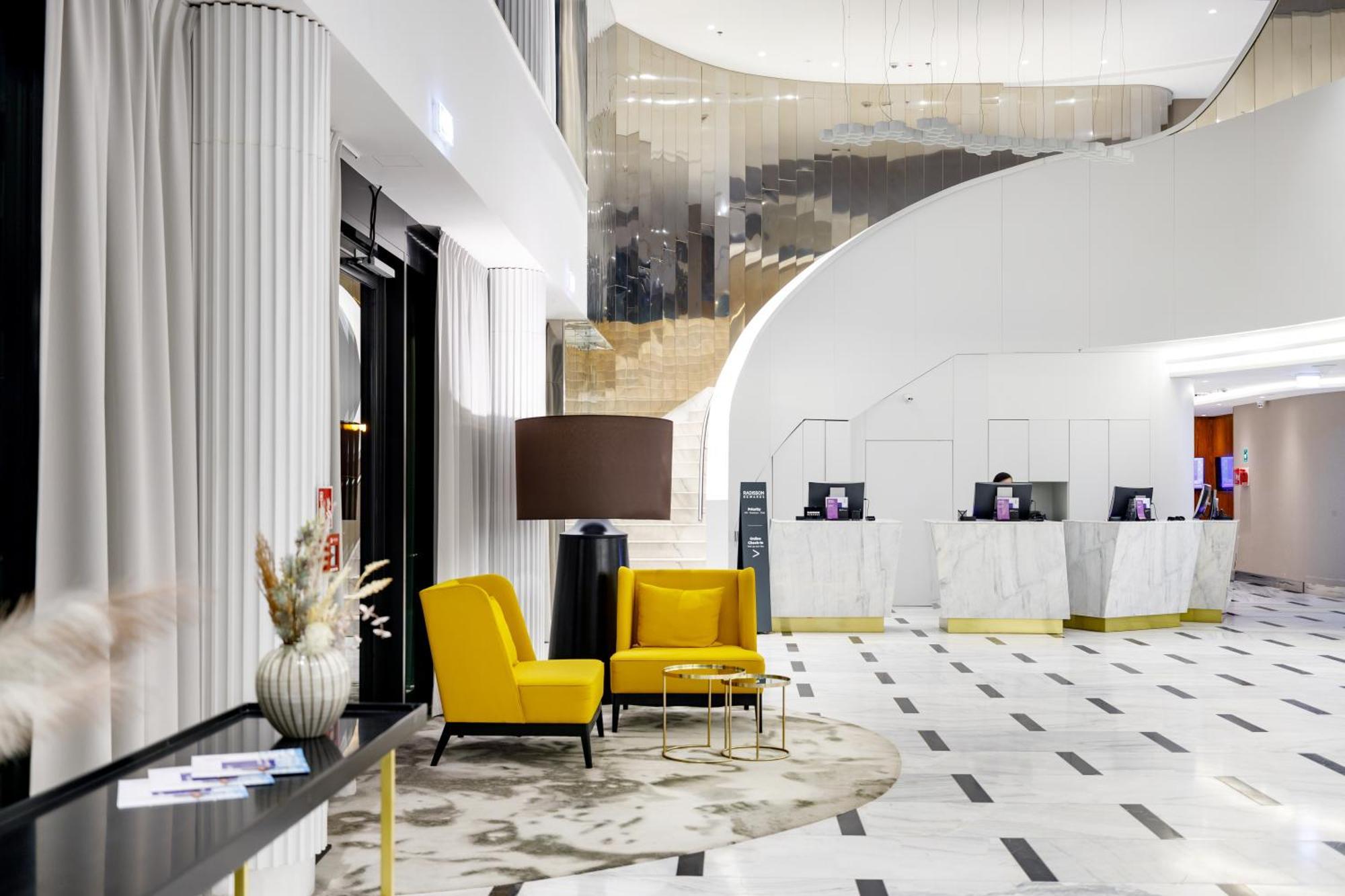 Radisson Blu Resort Świnoujście Εξωτερικό φωτογραφία The photo shows the interior of a modern hotel lobby. The space features a stylish design with a combination of yellow and neutral-colored seating, including two yellow armchairs and a small table. In the background, there is a reception area with ma