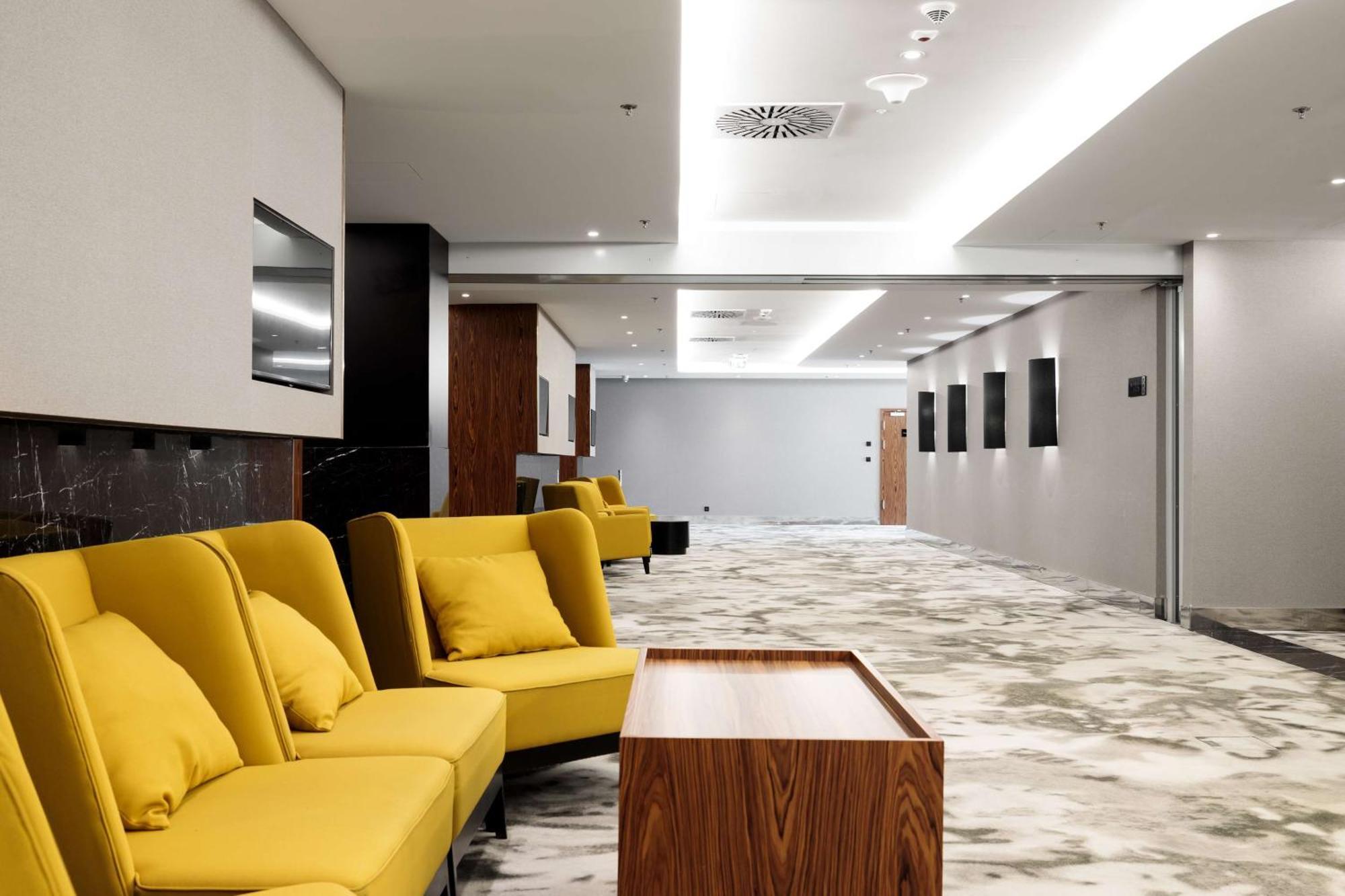 Radisson Blu Resort Świnoujście Εξωτερικό φωτογραφία The photo shows a modern interior space, likely a lobby or waiting area. There are several yellow sofas with cushions arranged in a casual seating area. In front of the sofas, there is a wooden coffee table. The flooring features a gray and white mar