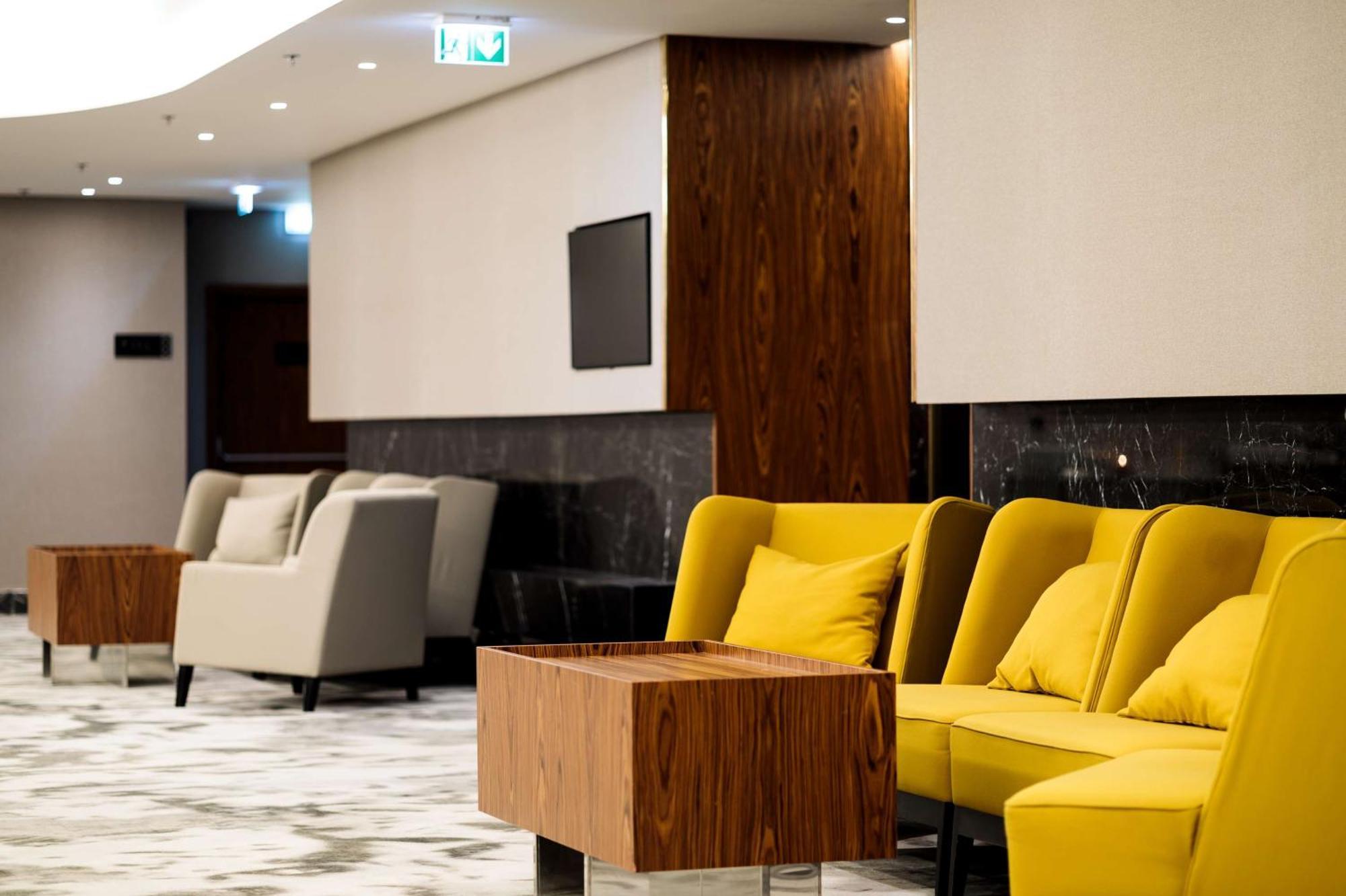 Radisson Blu Resort Świnoujście Εξωτερικό φωτογραφία The photo depicts a modern lounge or waiting area with stylish seating. On the left, there are soft gray armchairs arranged around a wooden coffee table. In the center, there are yellow chairs with plush cushions, contributing a vibrant contrast to t