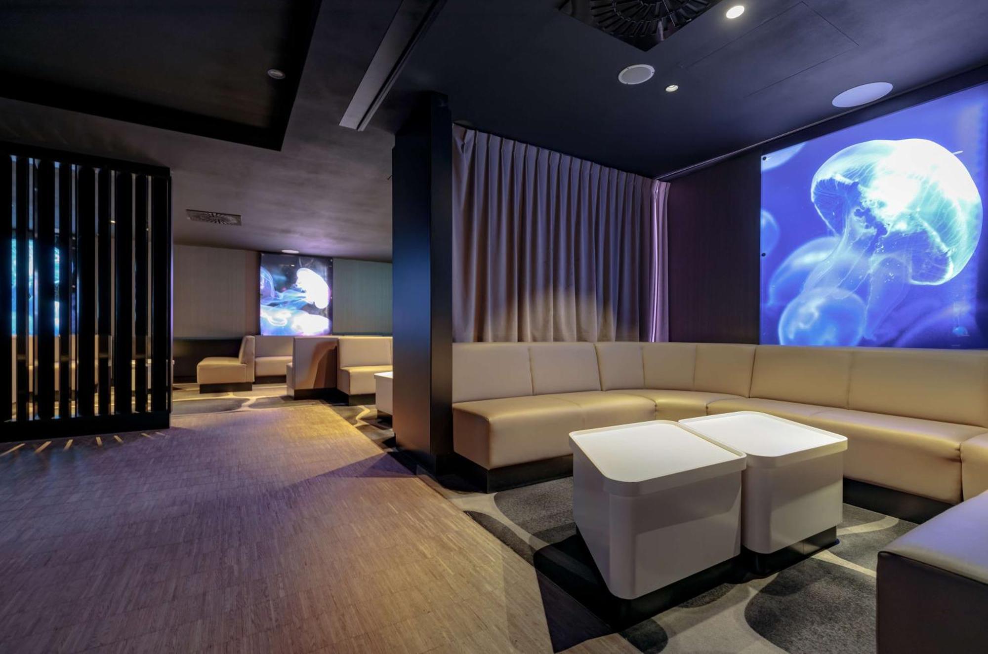 Radisson Blu Resort Świnoujście Εξωτερικό φωτογραφία The photo shows a modern interior space that appears to be a lounge or relaxation area. The design is sleek and minimalist, featuring a curved, light-colored seating arrangement with low tables at the center. The walls are dark, contributing to a coz