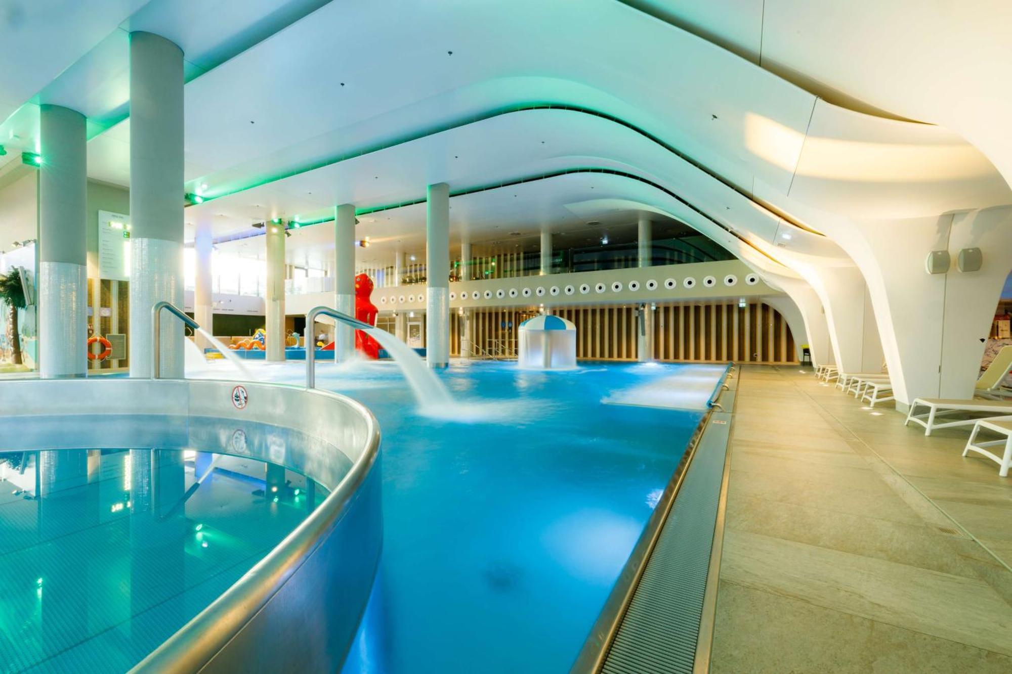 Radisson Blu Resort Świnoujście Εξωτερικό φωτογραφία The photo shows a modern indoor swimming pool area with an elegant design. The pool features curved edges and is filled with clear, blue water. There are various amenities, such as jets for relaxation and possibly seating areas along the edges. The l