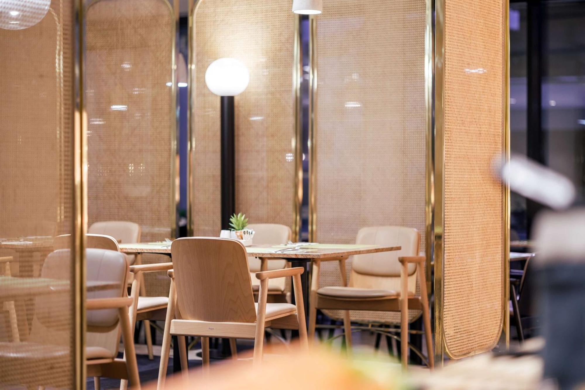 Radisson Blu Resort Świnoujście Εξωτερικό φωτογραφία The image shows an interior space, likely part of a restaurant or café. There are several wooden chairs arranged around tables, and the overall decor features soft lighting and warm colors. The walls appear to be partially covered with a woven materi