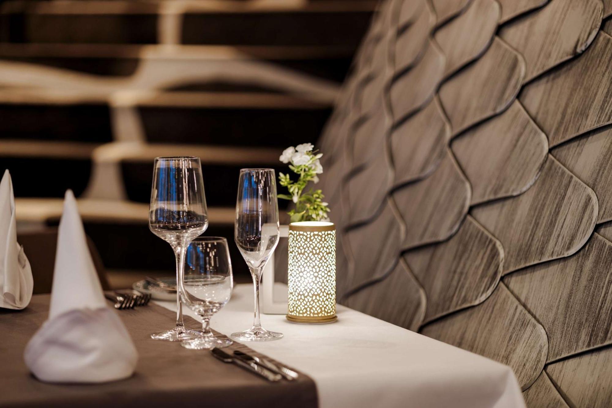 Radisson Blu Resort Świnoujście Εξωτερικό φωτογραφία The photo shows a beautifully arranged table setting in a restaurant. There are two elegant wine glasses and a smaller glass, likely for water, placed on a crisp white tablecloth. A decorative lantern with intricate designs holds a small flower arran