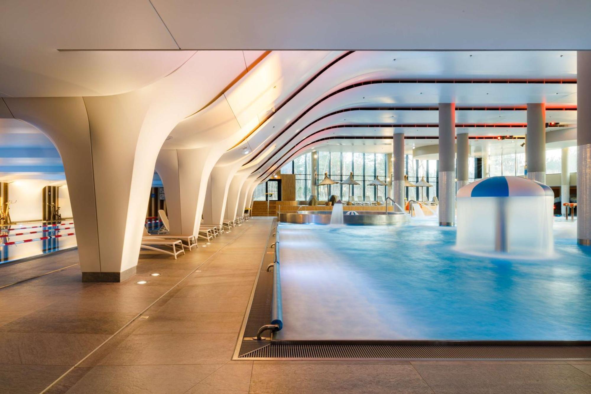 Radisson Blu Resort Świnoujście Εξωτερικό φωτογραφία The photo shows an indoor swimming pool area with a modern architectural design. The space features large windows allowing natural light to enter, and the interior has smooth, flowing lines in the ceiling and columns. The pool has a light blue water 