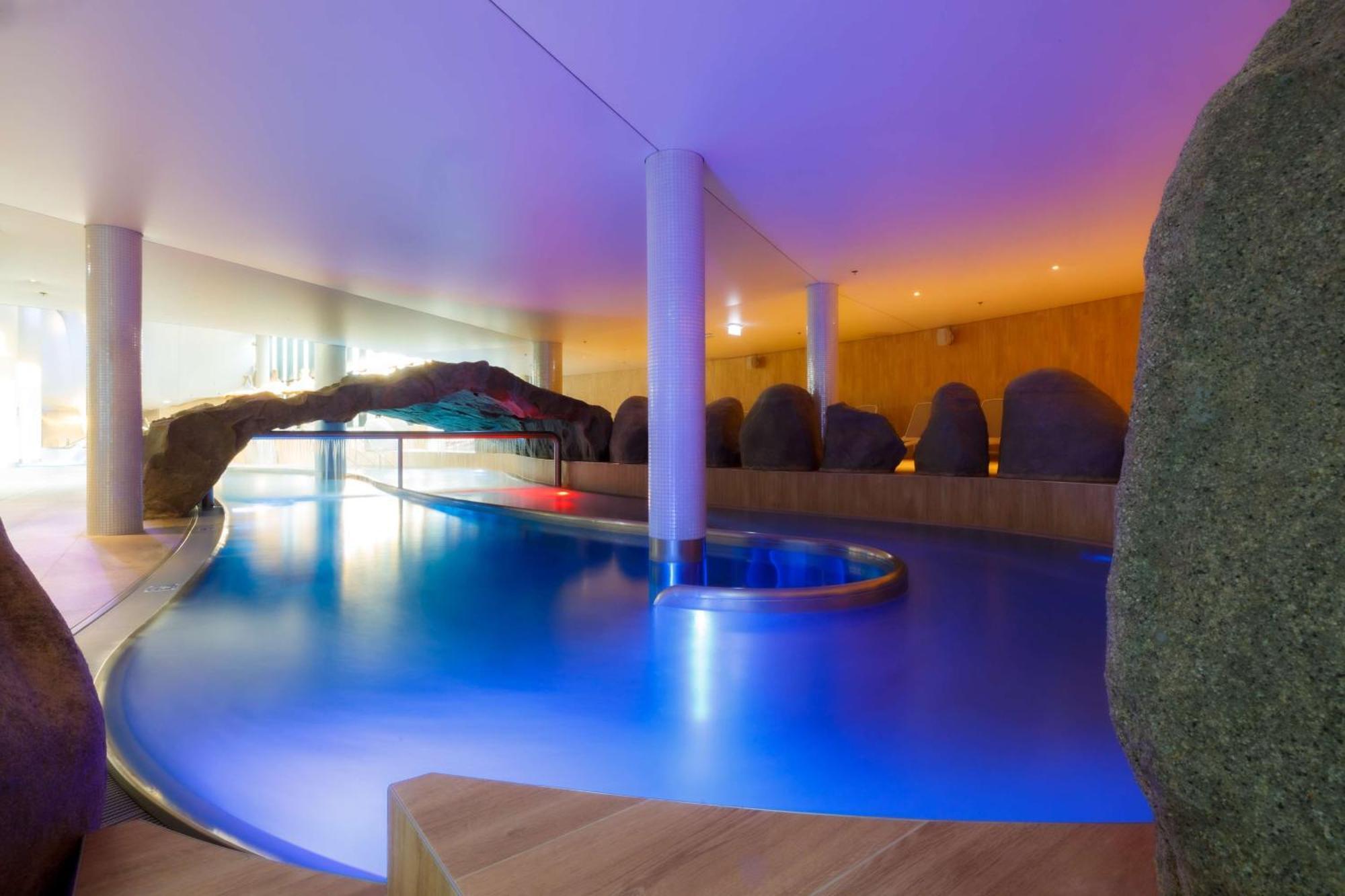 Radisson Blu Resort Świnoujście Εξωτερικό φωτογραφία The photo showcases an elegant indoor swimming pool area. The pool has a flowing, organic shape and is illuminated with soft blue and purple lighting, creating a calming ambiance. Surrounding the pool are smooth, natural-looking stones and wooden ele